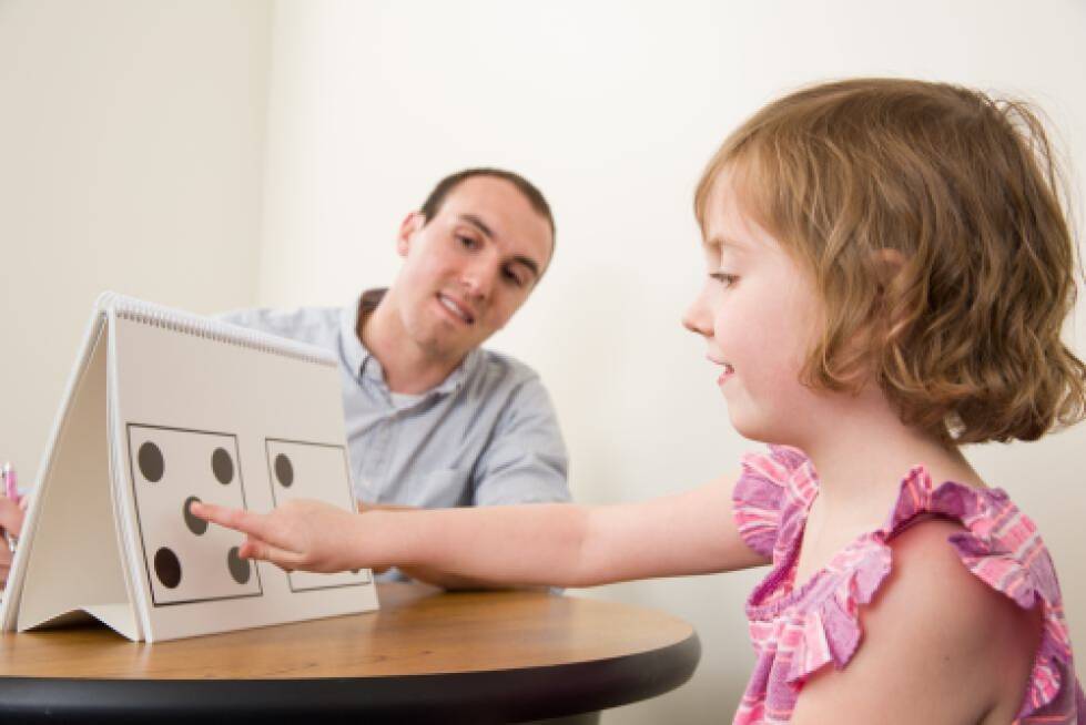 Researcher giving test to young child pointing at a domino